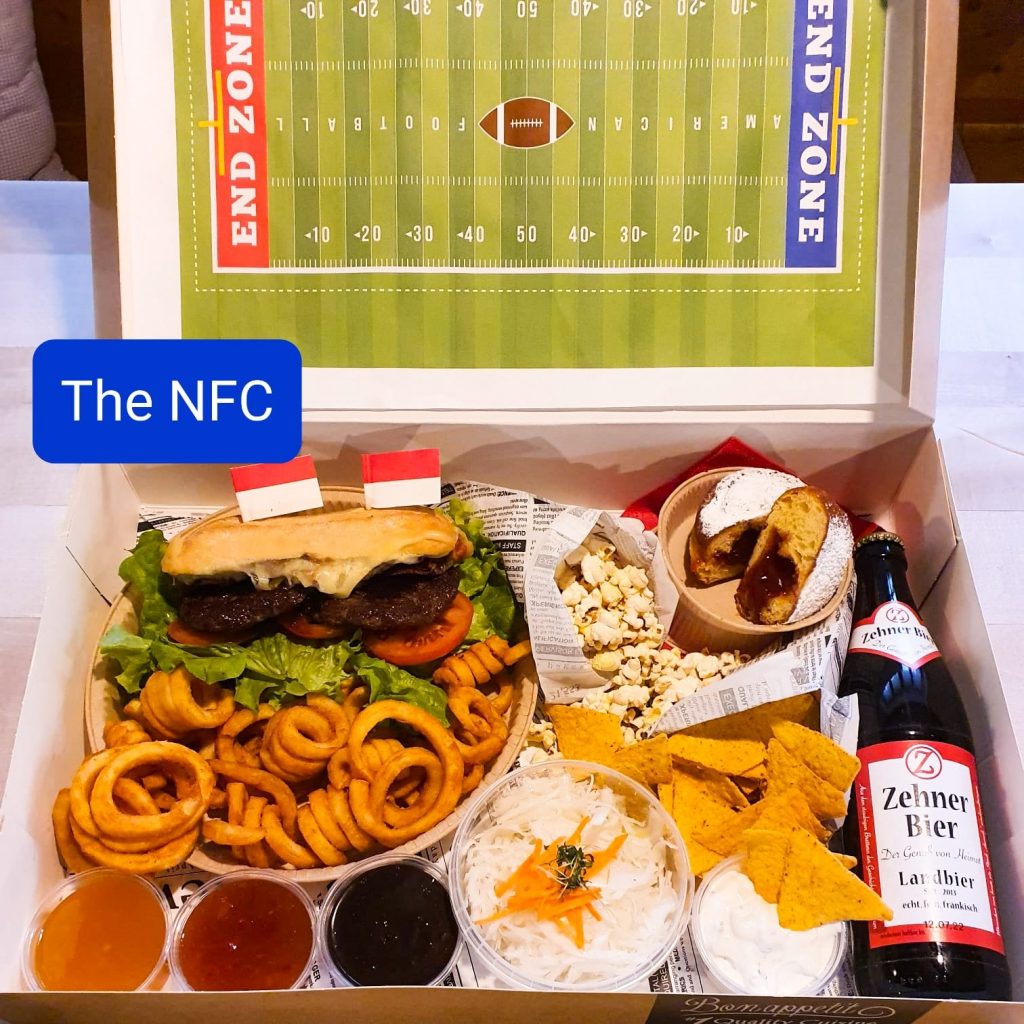Super-Bowl-Box der NFC mit Burger, Curly Fries, Dips und Zehner Bier