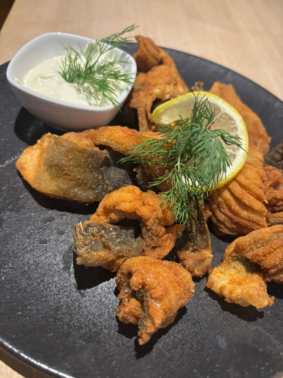 Knusprige Karpfenchips mit Zitrone, Dill und Dip auf einem dunklen Teller