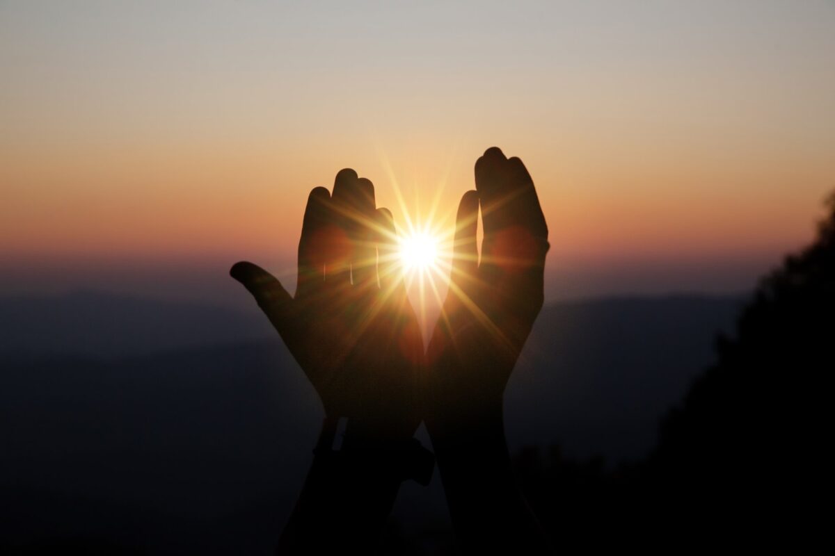 Hände halten Sonnenstrahlen im Sonnenuntergang - Symbol für den Heiligen Geist zu Pfingsten