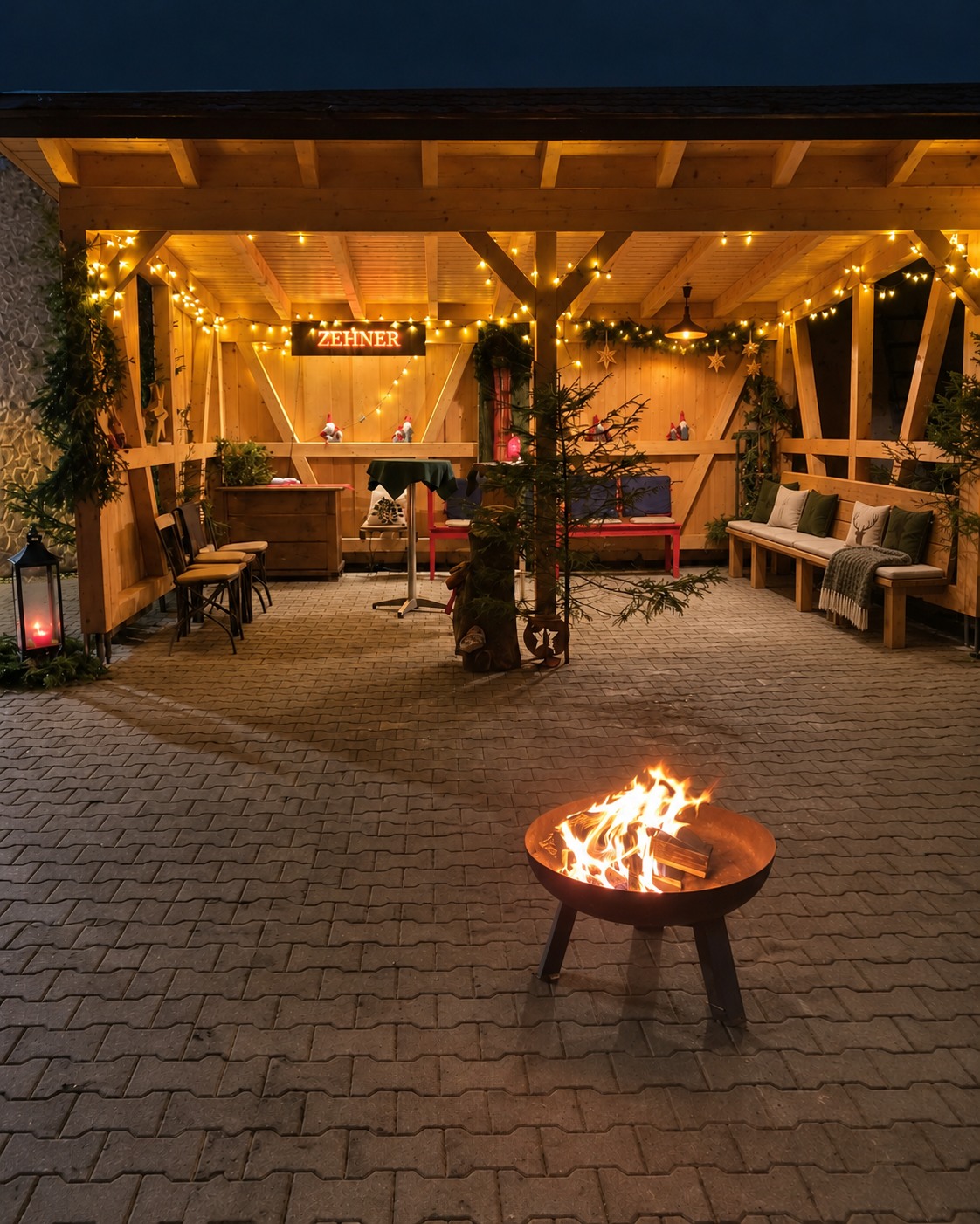 Blick in die Weihnachtshütte mit gepolsterter Holzbank, Tannengirlande, warmen Lichtern und Feuerschale